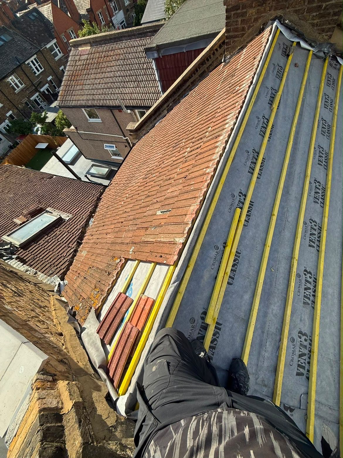 Roof half stripped, with old clay tiles on one side and new membrane and battens on the other