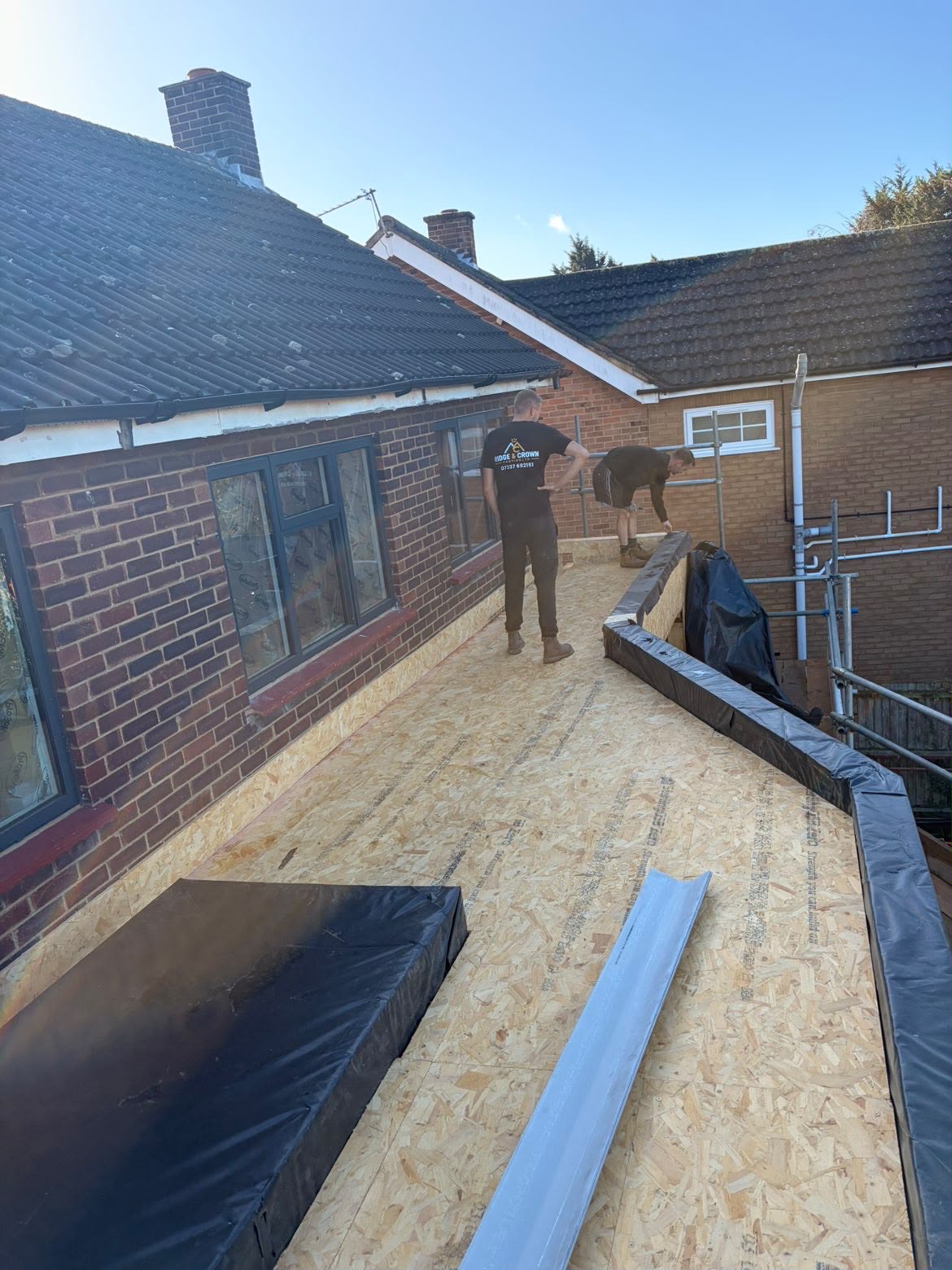 Flat roof extension deck being laid beside the pitched main roof of a house